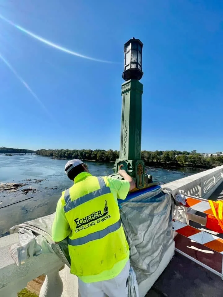 An ECHERER painter restores a historic bridge lamp post high over the river