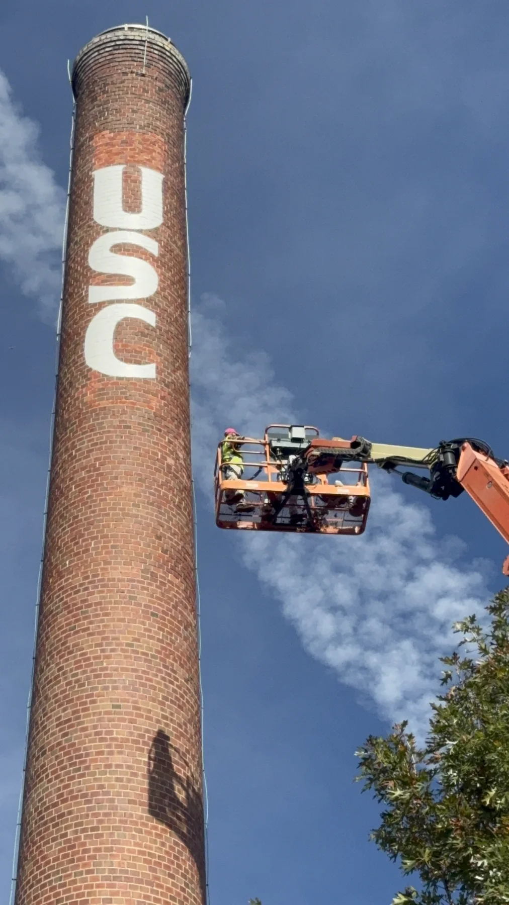 The full USC smokestack rising over the trees as an ECHERER crew paints from a boom lift, Columbia, SC